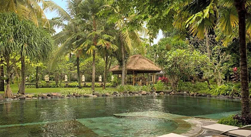 A lagoon-style pool at Segara Village Hotel, ringed by palm trees and tropical gardens with a thatched pavilion behind